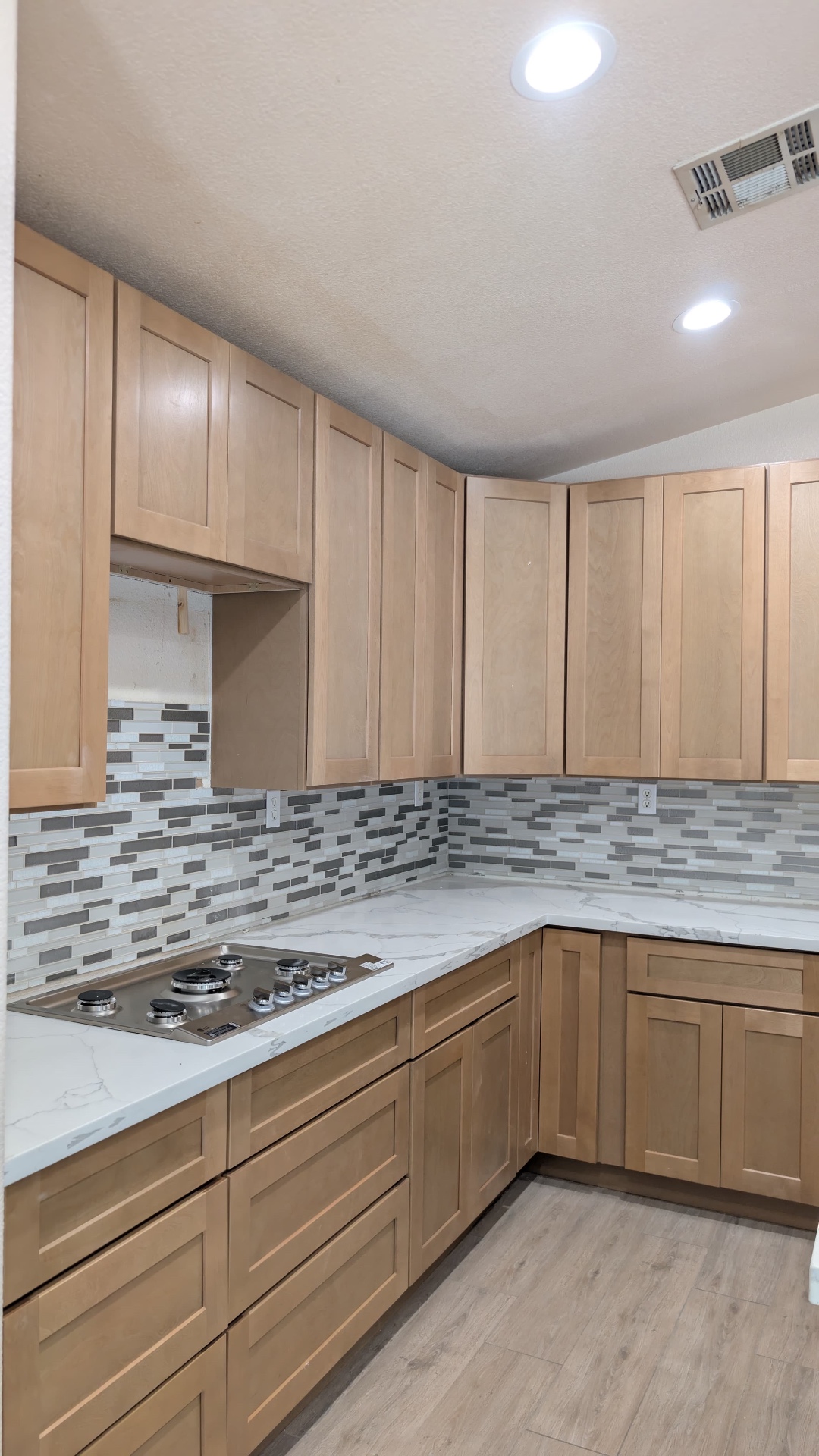 Close-up of stainless cooktop, calacatta quartz and grey-blue glass mosaic backsplash
